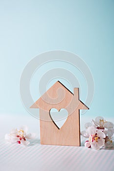 Closeup wooden house with hole in form of heart surrounded by white flowering tree branches on pastel blue background