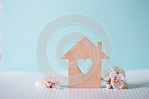 Closeup wooden house with hole in form of heart surrounded by white flowering tree branches on pastel blue background