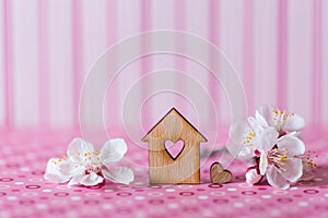 Closeup wooden house with hole in form of heart surrounded by white flowering tree branches on pink striped background