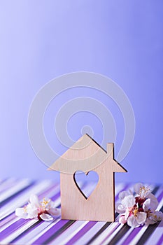 Closeup wooden house with hole in form of heart surrounded by white flowering tree branches on purple background