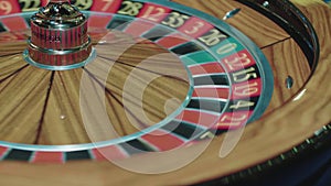 Closeup of wooden roulette wheel rotating in foreground. Table in luxury casino