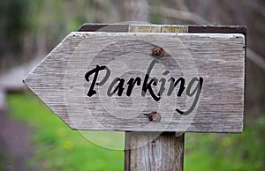 Closeup of a wooden sign with the [parking] word written on it against a blurry background