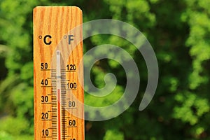 Closeup a wooden thermometer against green foliage showing high temperature
