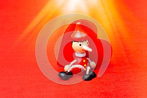 Closeup of a wooden toy Pinocchio sitting against a red wooden heart with bright beams overhead