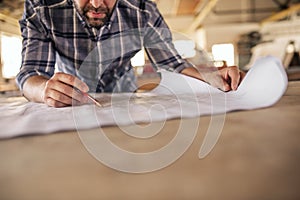 Woodworker leaning on a bench reading furniture design blueprints