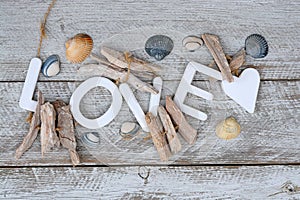 Closeup of the word love with seashells and wooden shaped heart isolated on the wooden surface