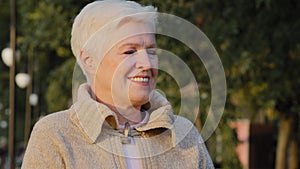 Closeup wrinkled face of 65s happy elderly woman outdoors looking aside having wide smile, dental implants and