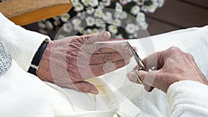 Closeup of wrinkled female hands cutting fingernail