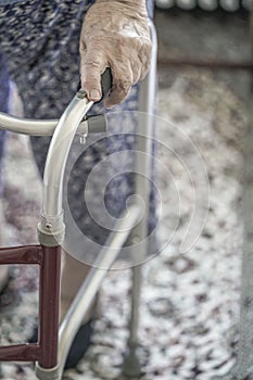 Wrinkled hand of an old woman holding on to a walker at home