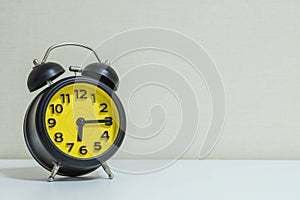 Closeup yellow and black alarm clock for decorate show a quarter past six or 6:15 a.m.on white wood desk and cream wallpaper textu