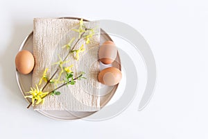 Closeup of yellow blooming Forsythia flowers, earthenware plate, beige napkin, and egg. Floral composition, feminine