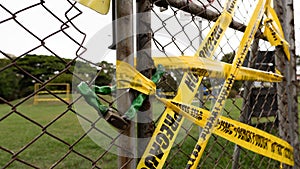 Closeup of a yellow precaution tape on a rusty chain-link fence in a park under a cloudy sky
