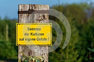 Closeup, of a yellow warning sign with German text `Entering the crops at your own risk`