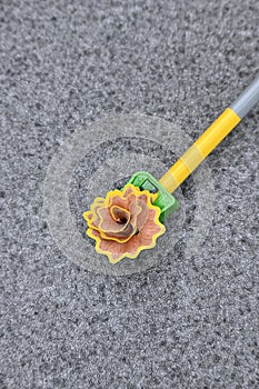 Closeup the yellow wooden pencil with green sharpener and waste flower over out of focus grey background