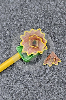 Closeup the yellow wooden pencil with green sharpener and waste flower over out of focus grey background