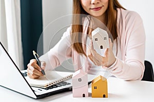Closeup of young Asian female hand choosing pink color house model after search for information on the Internet on white table at