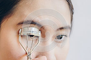 Closeup of young Asian woman using eyelash curler.