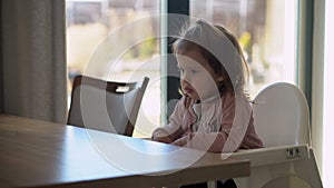 Closeup of young baby in white feeding high chair, kid is trying to eat himself, happy child with food stained face