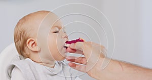 Closeup of young baby in white high baby chair and father's hand with a cake, while he is feeding the baby, who