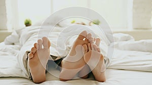 Closeup of young beautiful and loving couple hug and play their feet each other under blanket while wake up in bed in