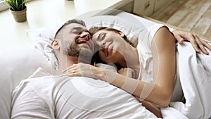 Closeup of young beautiful and loving couple talk and hug into bed while waking up in the morning.