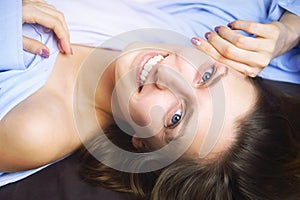 Closeup of young beautiful smiling woman in blue lying in bed. Natural beauty.