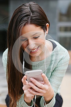 Closeup of a young beautiful woman listening to music with phone in outdoors.