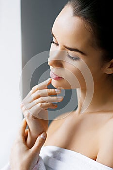 Closeup of a young beautiful woman with nude makeup touching her face. Beauty, spa. Holding Moisturizing Lotion. Skin Care Concept