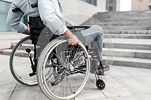 Closeup of young black man in wheelchair in front of stairs without ramp, having no possibility to enter building photo