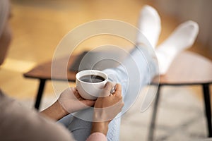 Closeup of young black woman warming her hands on cup of coffee, relaxing at home, empty space