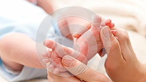 Closeup of young caring and loving mother massaging and stroking little feet of her newborn baby son lying in bed