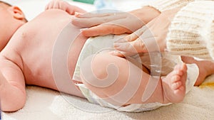 Closeup of young caring mother changing diaper of her newborn baby son lying on changing table at bedroom. Concept of