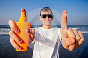 Closeup of a young caucasian man wearing a white T-shirt applying sunscreen to his body against the sea ocean