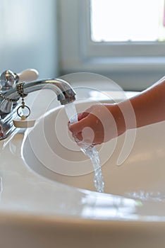 Closeup of young child washing hands under running water at the