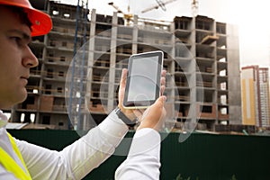 Closeup of young construction engineer on building site using di