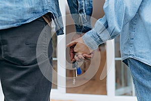 Closeup of young couple holding hands and new house key. couple standing back to back and holding keys to new house