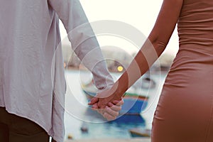 Closeup of young couple holding hands while walking on holiday, near the sea