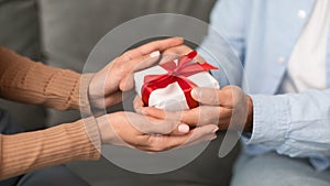 Closeup of young couple& x27;s hands holding wrapped gift box indoors