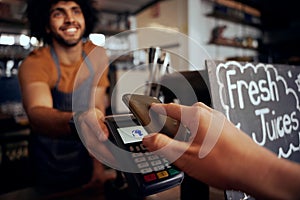 Closeup of young female hand making contactless payment in cafe using smartphone with waiter holding machine