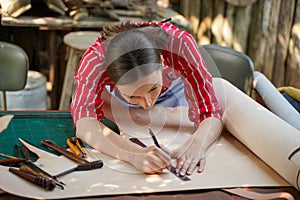 Closeup young female leather goods maker is drawing a design on leather in leather workshop