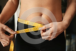 Closeup of a young female measuring her waist with a measuring tape - the concept of weight loss