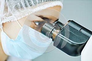 Closeup young female medic looking in microscope doing research in laboratory