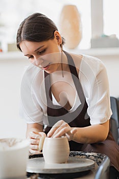 Closeup of young female potter with sponge keeping it close to rotating clay pot while shaping form of pot during work