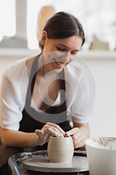 Closeup of young female potter with sponge keeping it close to rotating clay pot while shaping form of pot during work