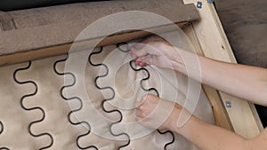 Closeup of a young girl is trying to repair the spring of the sofa. Heavy assembly of home furniture by yourself. Diy