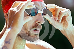 Closeup young handsome man, professional swimmer in goggles and swimming cap getting ready to swim, outdoors. Sport