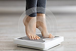 Closeup of young Indian woman standing on scales, measuring her weight indoors