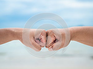 Closeup young man fist bump on the blue sky sea background. Friendship & Teamwork Concept.