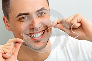 Closeup of young man flossing his teeth. Cleaning teeth with den