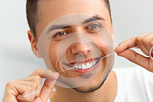 Closeup of young man flossing his teeth. Cleaning teeth with den